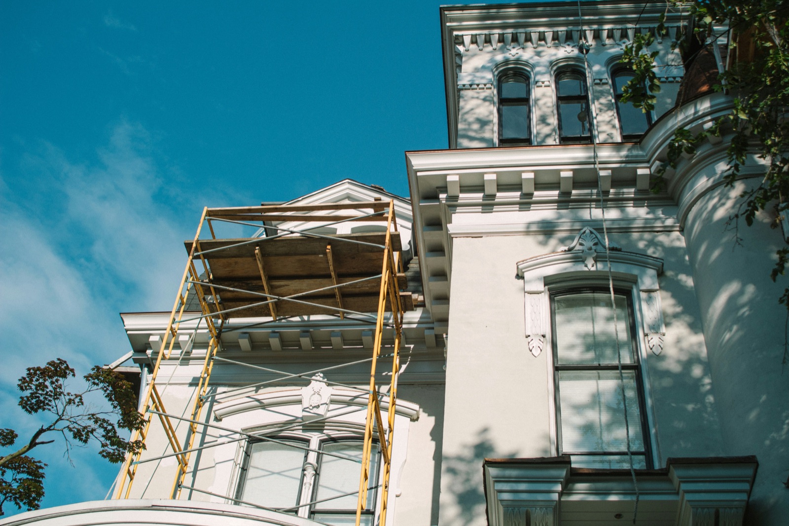 Scaffolding set up against the upper facade of a white Victorian-style home under a clear blue sky